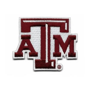 Könnte beinhalten: Gestickter Aufnäher mit den Buchstaben "ATM" in Burgunderrot und Weiß. Die Buchstaben sind in einem kräftigen Blockstil mit weißem Rand gehalten. Der Aufnäher ist für Kleidung oder Accessoires bestimmt.