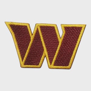 May include: Embroidered patch featuring a maroon "W" with a gold outline. The patch has a textured appearance, with the letter taking up most of the frame. The design is simple and bold, suitable for application on various fabrics.