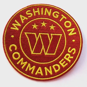 Könnte beinhalten: Ein kreisförmiger, gestickter Aufnäher mit den gelben Worten "WASHINGTON COMMANDERS", die ein gelbes Doppel-"W"-Logo und drei Sterne umgeben, alles auf rotem Grund. Der Aufnäher ist ein Sportteam-Emblem.