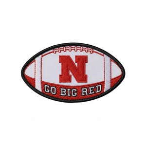 May include: Embroidered patch in the shape of a football. The patch features a white background with a large red "N" in the center. The words "GO BIG RED" are printed in red at the bottom. The patch is outlined in black.