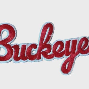 Op de afbeelding: Geborduurde patch met het woord "Buckeyes" in rode letters, omrand met wit. Deze patch is bedoeld om op kleding of accessoires te naaien of te strijken.