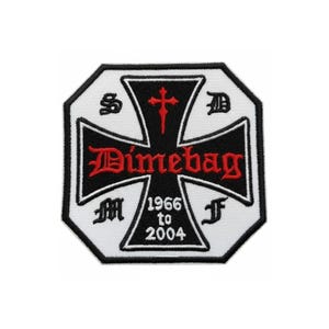 Puede incluir: Parche bordado en blanco y negro con un diseño de cruz y la palabra "Dimebag" en rojo. El parche también incluye los años "1966 a 2004" y varios símbolos.