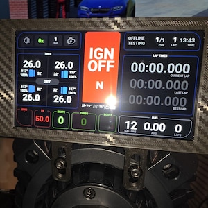 May include: A digital racing dashboard with a carbon fiber frame displays real-time vehicle data. The screen shows lap times, fuel levels, and engine diagnostics. The IGN OFF indicator is prominently displayed in orange.