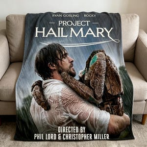 Puede incluir: Una manta gris con el título de la película "Project Hail Mary" con Ryan Gosling y Rocky. La imagen en la manta muestra a un hombre con una camisa blanca sosteniendo un objeto grande y marrón bajo la lluvia. La manta está sobre un sofá beige.