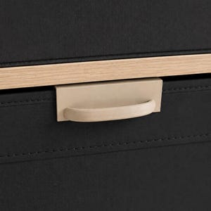 May include: A black fabric storage drawer featuring a light-colored wooden trim along the top edge and a matte beige metal handle centered on the front panel. The drawer is constructed with visible stitching along the horizontal seam.