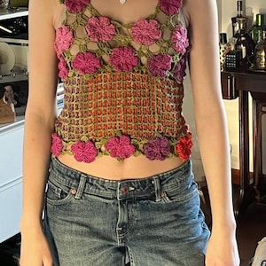 May include: A green crochet top with pink and red flowers. The top has a loose fit and is sleeveless. It is made of a lightweight material and would be perfect for warm weather.