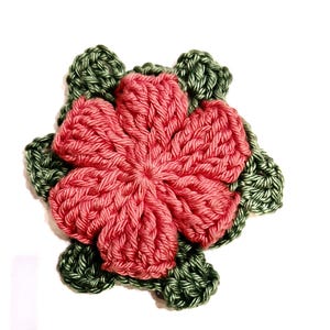 Op de afbeelding: Een gehaakte bloem met een roze hart en groene bladeren.