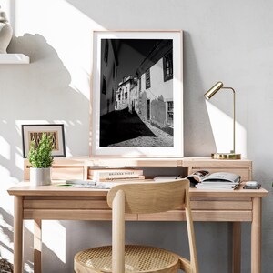 Large Portugal photography print leaning on a wooden desk with a gold lamp. Modern home office decor with minimalist travel art.