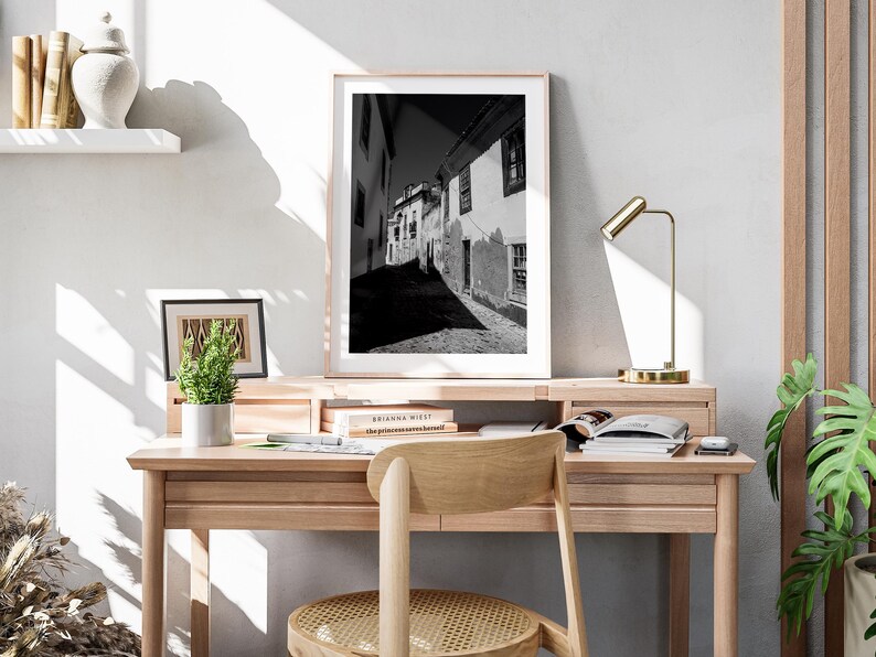 Large Portugal photography print leaning on a wooden desk with a gold lamp. Modern home office decor with minimalist travel art.