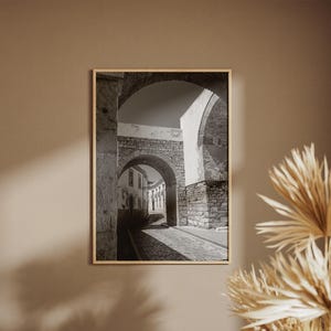 Historic Portugal archway print hanging on a beige wall next to dried palm leaves. Neutral boho home decor inspiration for a warm entryway or hallway.