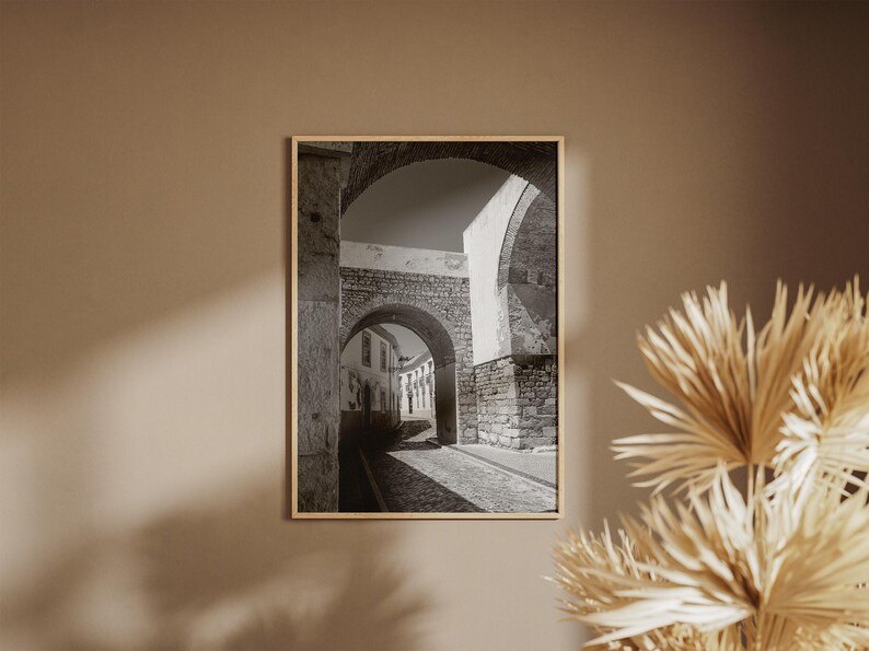 Historic Portugal archway print hanging on a beige wall next to dried palm leaves. Neutral boho home decor inspiration for a warm entryway or hallway.