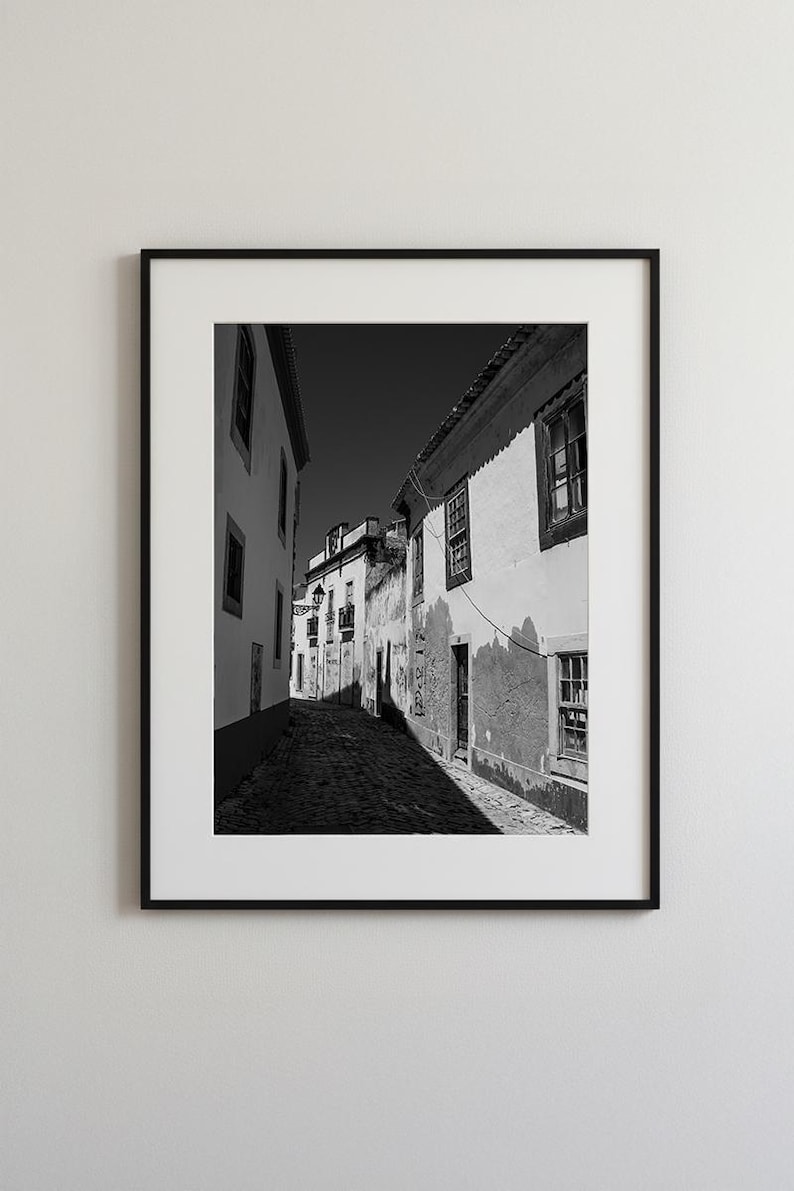 Black and white framed wall art of a narrow cobblestone street in Faro Old Town, Portugal. Rustic European architecture print.