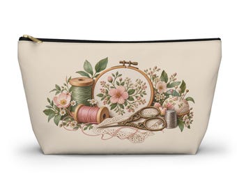 May include: A beige zippered pouch featuring a printed illustration of sewing supplies including a wooden embroidery hoop with floral stitching, green and pink thread spools, ornate metal scissors, a thimble, and lace.