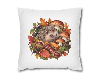 May include: A square white throw pillow featuring a central illustration of a brown hedgehog surrounded by autumn leaves, brown mushrooms, dark blackberries, and spiky chestnut husks containing smooth brown chestnuts.