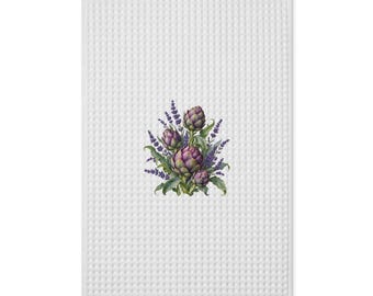 May include: A white waffle-weave kitchen towel featuring a central botanical illustration of purple artichokes surrounded by sprigs of lavender. The rectangular textile has a textured grid pattern throughout its surface.