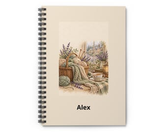May include: A spiral-bound notebook with a cream-colored cover featuring a printed illustration of a woven basket filled with yarn, knitting needles, and lavender sprigs next to a teacup. The name Alex is printed in black text below the image.