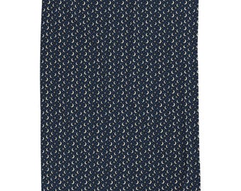 Peut inclure: Une couverture en tissu rectangulaire présentant un fond bleu marine foncé avec un motif répétitif de petits croissants de lune blancs et de minuscules étoiles dorées répartis uniformément sur toute la surface du textile.