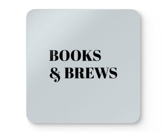 Puede incluir: Un posavasos cuadrado de color gris claro con esquinas redondeadas que presenta el texto negro BOOKS & BREWS centrado en la superficie. El diseño utiliza una fuente serif en negrita para las palabras y un símbolo ampersand estilizado.