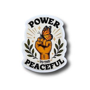 May include: A die-cut sticker featuring a raised fist in a warm orange tone with a monarch butterfly perched on the knuckles. The design includes green leafy branches on both sides and the black text POWER TO THE PEACEFUL in a bold font.
