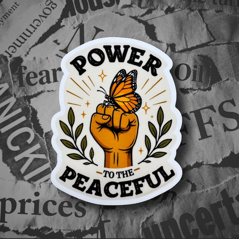 May include: A die-cut sticker featuring a raised fist in an orange-yellow hue with a monarch butterfly perched on top. The design includes green leafy branches on both sides and the black text POWER TO THE PEACEFUL arched above and below the fist.