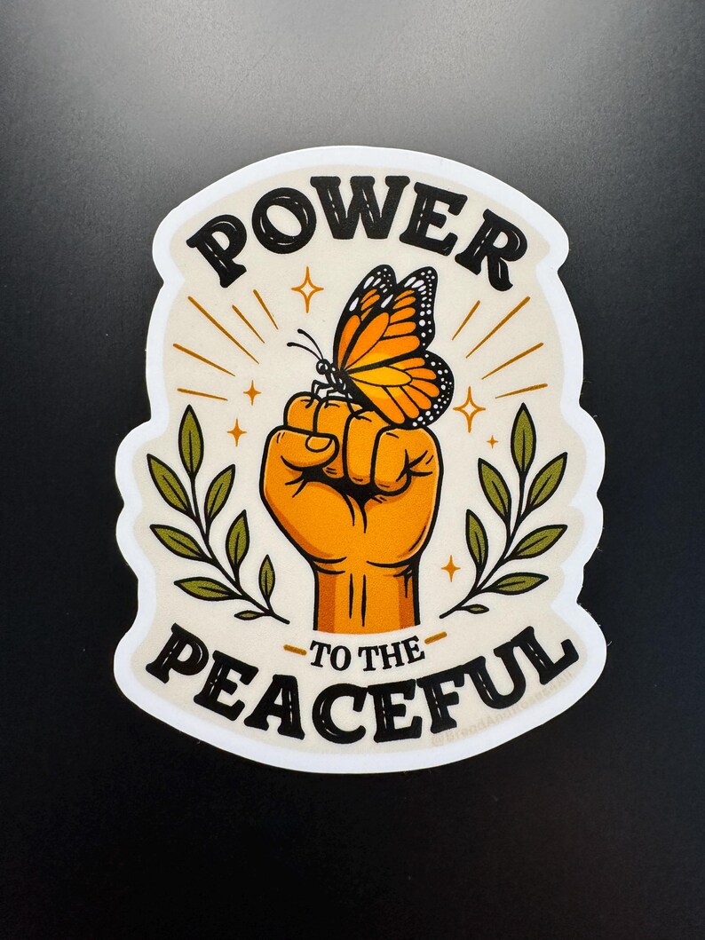 May include: A die-cut sticker featuring a raised fist in orange with a monarch butterfly perched on the knuckles. The design includes green leafy branches on both sides, gold star accents, and the black text POWER TO THE PEACEFUL on a cream background.