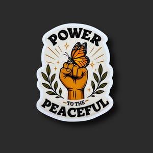 May include: A die-cut sticker featuring a raised fist with an orange monarch butterfly perched on the knuckles. The design includes green leafy branches on both sides and the black text POWER TO THE PEACEFUL arranged in a curved arch format.