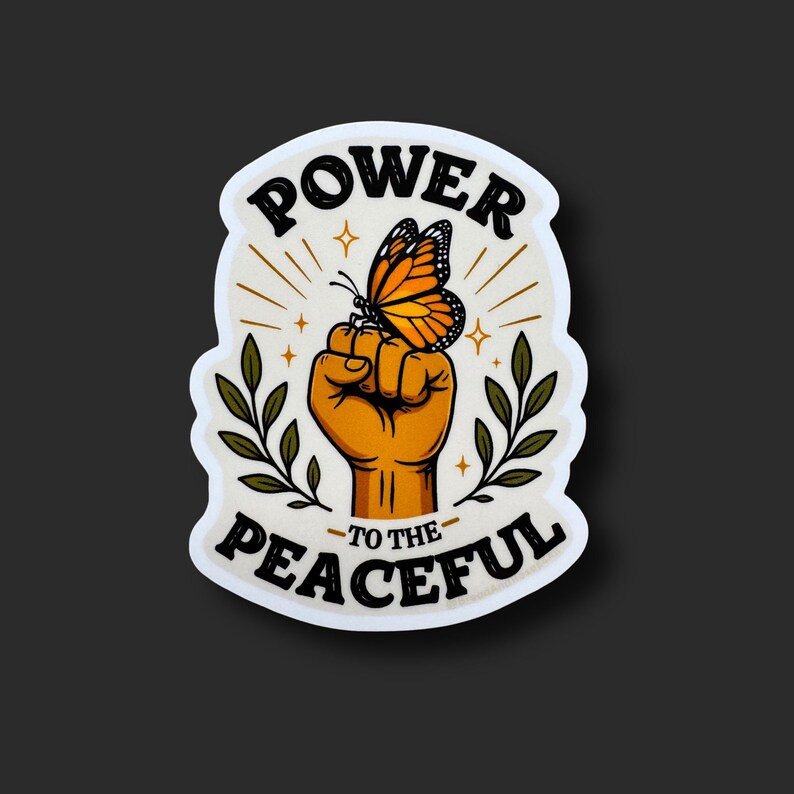 May include: A die-cut sticker featuring a raised fist with an orange monarch butterfly perched on the knuckles. The design includes green leafy branches on both sides and the black text POWER TO THE PEACEFUL arranged in a curved arch format.
