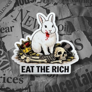 Pode incluir: Um adesivo recortado com um coelho branco com sangue vermelho no queixo, sentado sobre um crânio humano e ossos. Uma coroa dourada e uma cartola preta estão presentes. O texto EAT THE RICH está impresso em letras pretas maiúsculas.