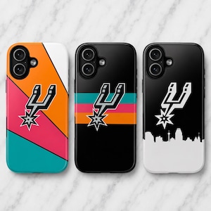 Peut inclure: Trois coques de téléphone arborant le logo des San Antonio Spurs. La première présente des rayures diagonales orange, rose et bleu sarcelle. La deuxième est noire avec des rayures horizontales. La troisième est noire avec une silhouette urbaine blanche.