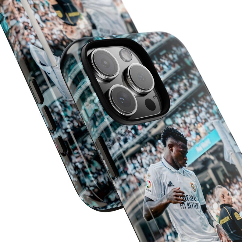 May include: A black phone case featuring a high-resolution graphic of a soccer player in a white jersey on a field. The case has a black camera cutout frame and black side buttons, showcasing a detailed stadium crowd scene in the background.