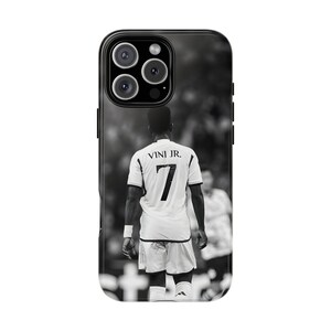 May include: A black and white smartphone case featuring a rear view of a soccer player wearing a jersey with the text VINI JR. and the number 7 on the back. The design shows the player standing on a field with a blurred stadium background.