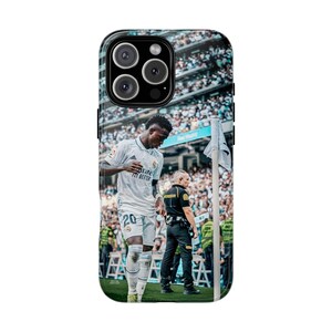 May include: A smartphone case featuring a high-resolution photograph of a soccer player in a white jersey with the number 20, standing on a field near a corner flag, with a stadium crowd and a security official visible in the background.