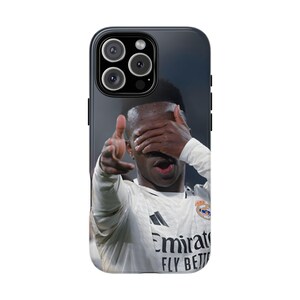May include: A black smartphone case featuring a photographic print of a soccer player in a white jersey with the text Emirates FLY BETTER. The player is shown with one hand covering their eyes and the other hand extended forward in a gesture.