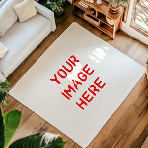 May include: A cream-coloured rectangular rug with the words "YOUR IMAGE HERE" in red. The rug is on a hardwood floor, with a white sofa, wooden furniture, and a window visible in the background. The rug is a focal point.