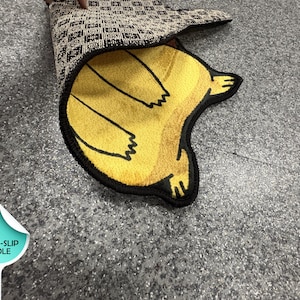 May include: A yellow rug with a black border and a cartoon bear paw design. The rug is partially rolled up, revealing a patterned underside. The rug is designed with a non-slip sole.
