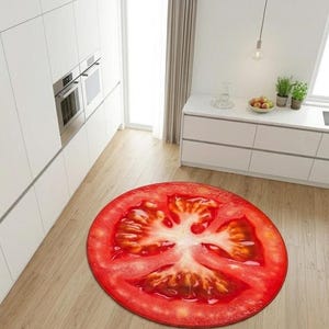May include: A circular rug featuring a detailed depiction of a tomato slice. The rug's design showcases red, white, and yellow hues, mimicking the internal structure of a tomato. It's positioned on a light wooden floor in a kitchen environment.