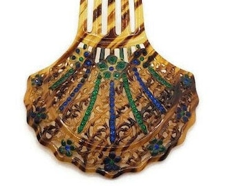 May include: A brown tortoiseshell hair comb with a decorative, scalloped design. The comb is adorned with blue, green, and gold accents.