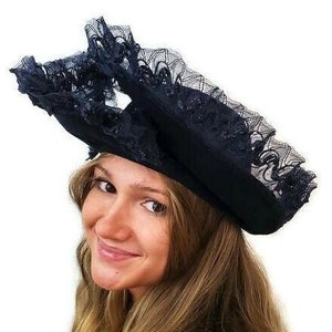 May include: A black lace hat with a wide brim and ruffled trim. The hat is worn by a person with long brown hair.