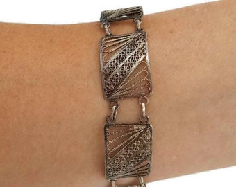 May include: A silver filigree bracelet with a delicate, intricate design. The bracelet is made of multiple connected rectangular links, each featuring a detailed pattern of interwoven lines.