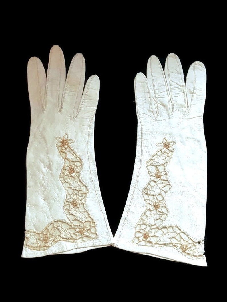 K&ouml;nnte beinhalten: Ein Paar wei&szlig;e Lederhandschuhe mit zartem wei&szlig;en H&auml;kelrand und Perlenakzenten.