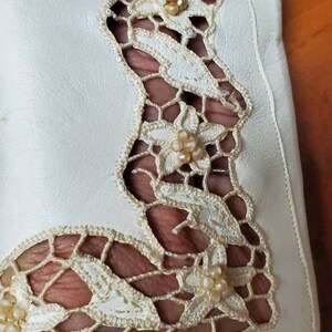 K&ouml;nnte beinhalten: Wei&szlig;er Lederhandschuh mit einem zarten Spitzendesign mit floralen Motiven und Perlenakzenten.