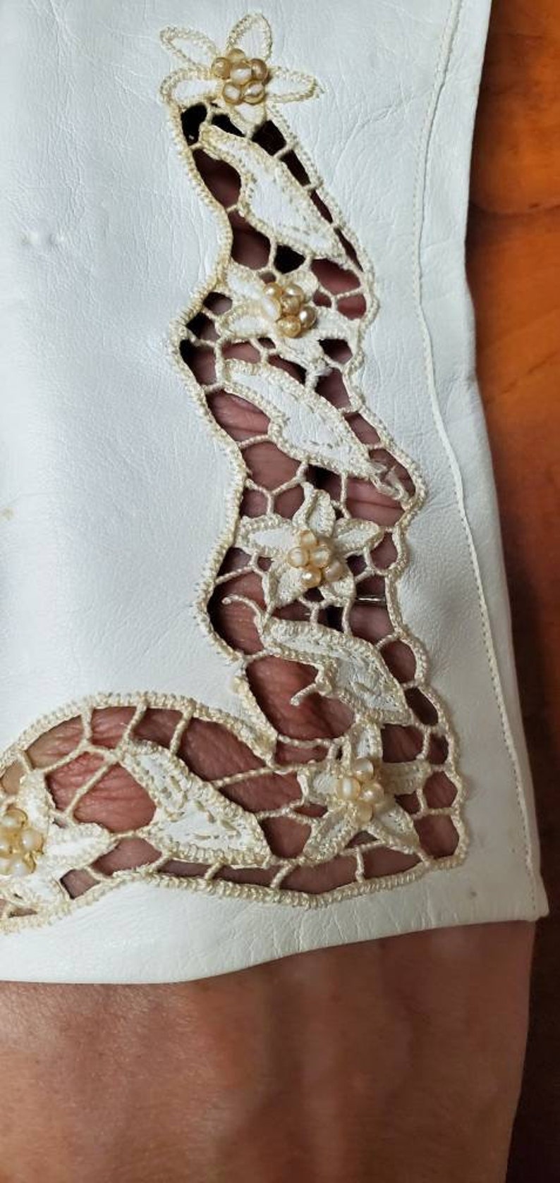 K&ouml;nnte beinhalten: Wei&szlig;er Lederhandschuh mit einem zarten Spitzendesign mit floralen Motiven und Perlenakzenten.