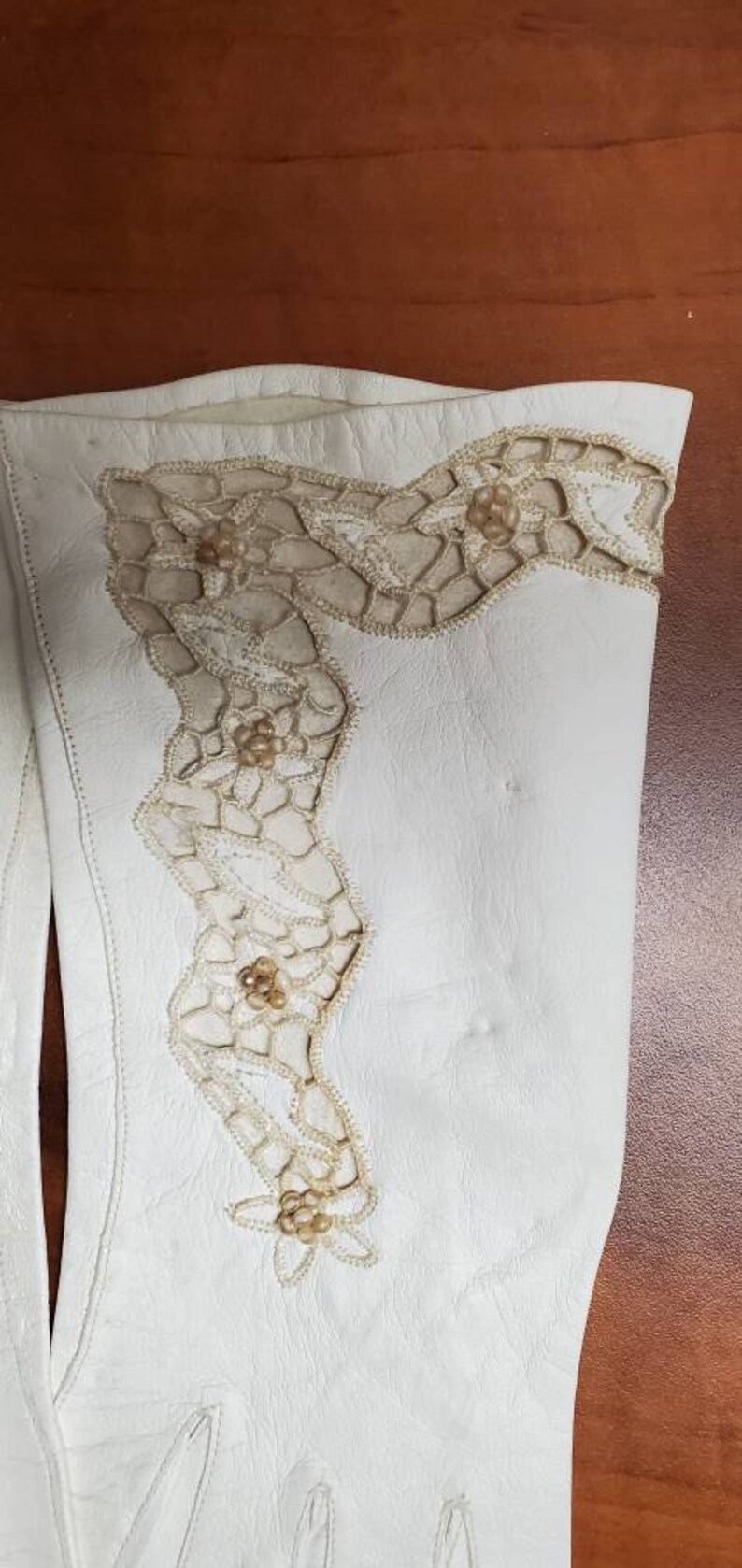 K&ouml;nnte beinhalten: Ein Paar wei&szlig;e Lederhandschuhe mit zarter Spitze und Perlenbesatz.