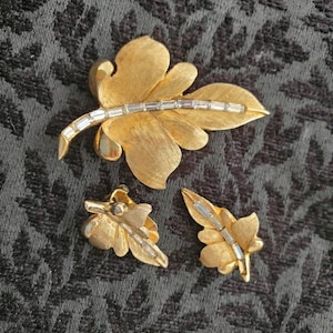 以下が含まれることがあります： クリアなラインストーンのアクセントが付いた、ゴールドの葉の形をしたブローチとマッチするイヤリングです。