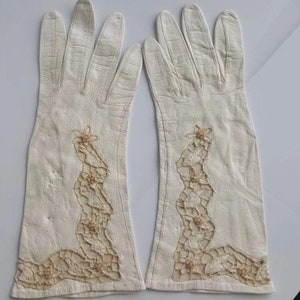 K&ouml;nnte beinhalten: Ein Paar wei&szlig;e Lederhandschuhe mit zarten Spitzen- und Perlenverzierungen. Die Handschuhe sind lang und reichen &uuml;ber das Handgelenk.