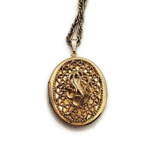 May include: A gold locket necklace with a filigree design. The locket is oval shaped and has a delicate chain.