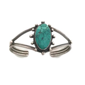 Może przedstawiać: Srebrna bransoletka z turkusowym kamieniem osadzonym w srebrnej oprawie. Bransoletka ma prosty design z jednym kamieniem i skręconym drutem.