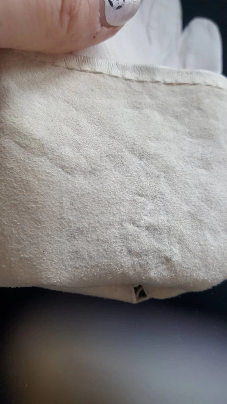 K&ouml;nnte beinhalten: Nahaufnahme einer wei&szlig;en Lederoberfl&auml;che mit subtiler Textur. Die Oberfl&auml;che scheint Teil eines Kleidungsst&uuml;cks oder Accessoires zu sein.