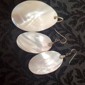 May include: Three white oval-shaped earrings with silver hooks and gold accents. The earrings are made of mother of pearl.