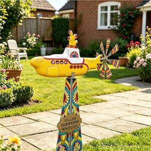 Puede incluir: Un molinillo de viento con forma de submarino amarillo con una hélice colorida y un soporte decorativo. El submarino tiene detalles rojos y blancos. El soporte muestra el texto "YELLOW SUBMARINE WHIRLIGIG".